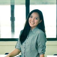 a woman in a gray shirt smiling in front of a window