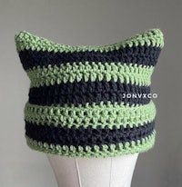 a green and black crocheted hat on a mannequin