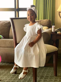 a little girl in a white dress sitting on a chair