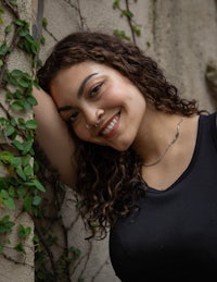 a woman with curly hair leaning against a wall