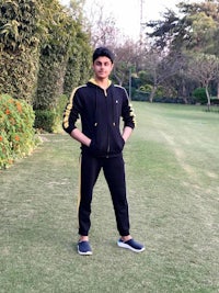 a young man in a black and yellow tracksuit standing in a grassy area