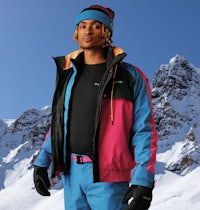 a man in a blue and pink ski suit standing in front of a snowy mountain