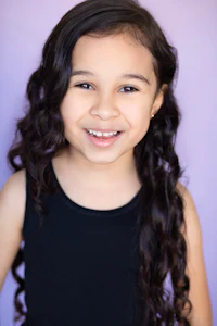a young girl with long curly hair smiling for the camera