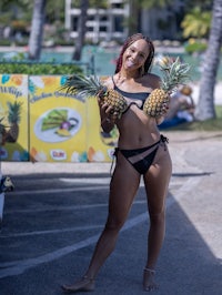 a woman in a bikini holding two pineapples