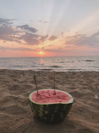 a bowl of watermelon on the beach at sunset