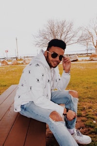 a man sitting on a bench wearing a white hoodie and ripped jeans