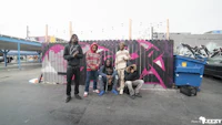 a group of people standing in front of a graffiti covered wall
