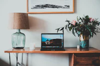 a laptop sits on a desk next to a vase