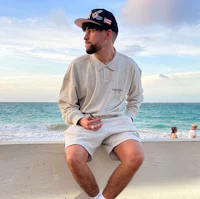 a man sitting on a wall next to the ocean wearing a hat and shorts