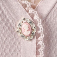 a close up of a pink cardigan with a cameo on it