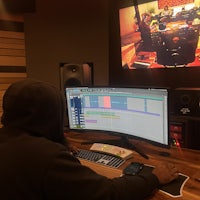 a man in a hoodie in front of a monitor in a recording studio
