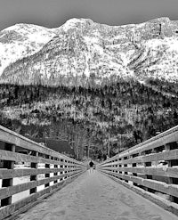 a black and white photo of a bridge with snowy mountains in the background