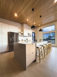 a modern kitchen with wooden ceilings and stools