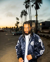 a man with dreadlocks standing on a beach with palm trees