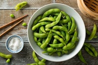a bowl of green soybeans and chopsticks on a wooden table