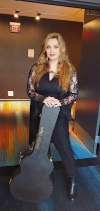 a woman holding an acoustic guitar in a hallway