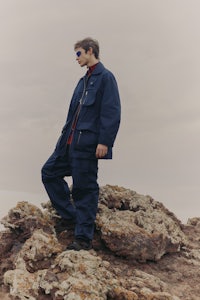 a man in a blue jacket standing on top of a rock