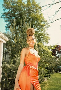 a woman in an orange dress posing in front of a house