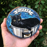 a person is holding a piece of wood with a black cat in a bowl
