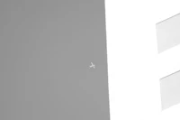 a black and white photo of a plane flying over a building