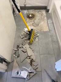 a bathroom with a broken floor and a yellow broom