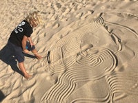 a young boy drawing a sand sculpture in the sand