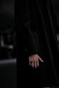 a man in a black coat walking down the runway