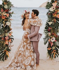 a bride and groom embrace under a floral arch on the beach