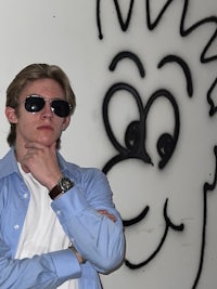 a young man wearing sunglasses in front of a graffiti wall