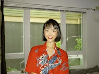a woman in a red shirt standing in front of a window