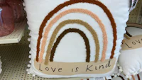 a pillow with a rainbow on it that says love is kind