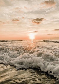 the sun is setting over a beach with waves