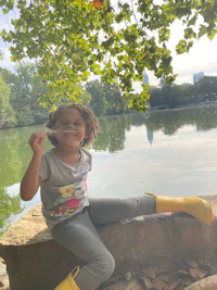 a little girl sitting on a rock next to a lake
