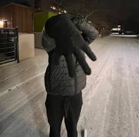 a man in a black jacket is holding his hand up in the snow