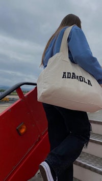 a woman carrying a tote bag with the word adola on it