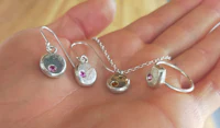a hand holding a pair of silver earrings and a silver necklace