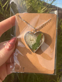 a person holding a heart shaped necklace with sand in it