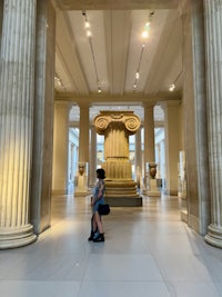 a woman walking through a museum with columns
