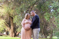 a pregnant man and woman standing in a park