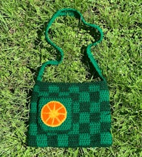 a green crocheted bag with an orange on it