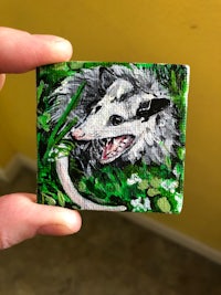 a person holding a small painting of an opossum