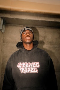 a man in a black hoodie standing in front of a wall