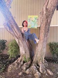 a woman sitting in a tree holding a painting
