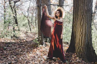 a woman in a burgundy dress standing in the woods