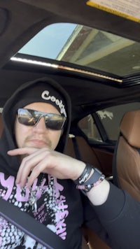 a man in a hoodie and sunglasses sitting in a car