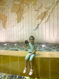 a young girl sitting on a wall in front of a world map