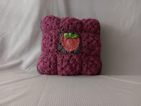 a purple crocheted pillow with a strawberry on it