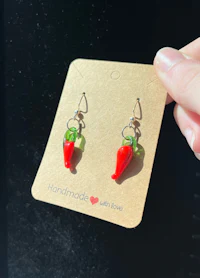 a person holding a pair of earrings with red and green peppers