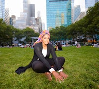 a woman in a hijab sitting on the grass in a park