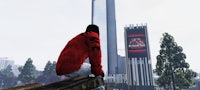 a man in a red jacket is sitting on a log in front of a skyscraper